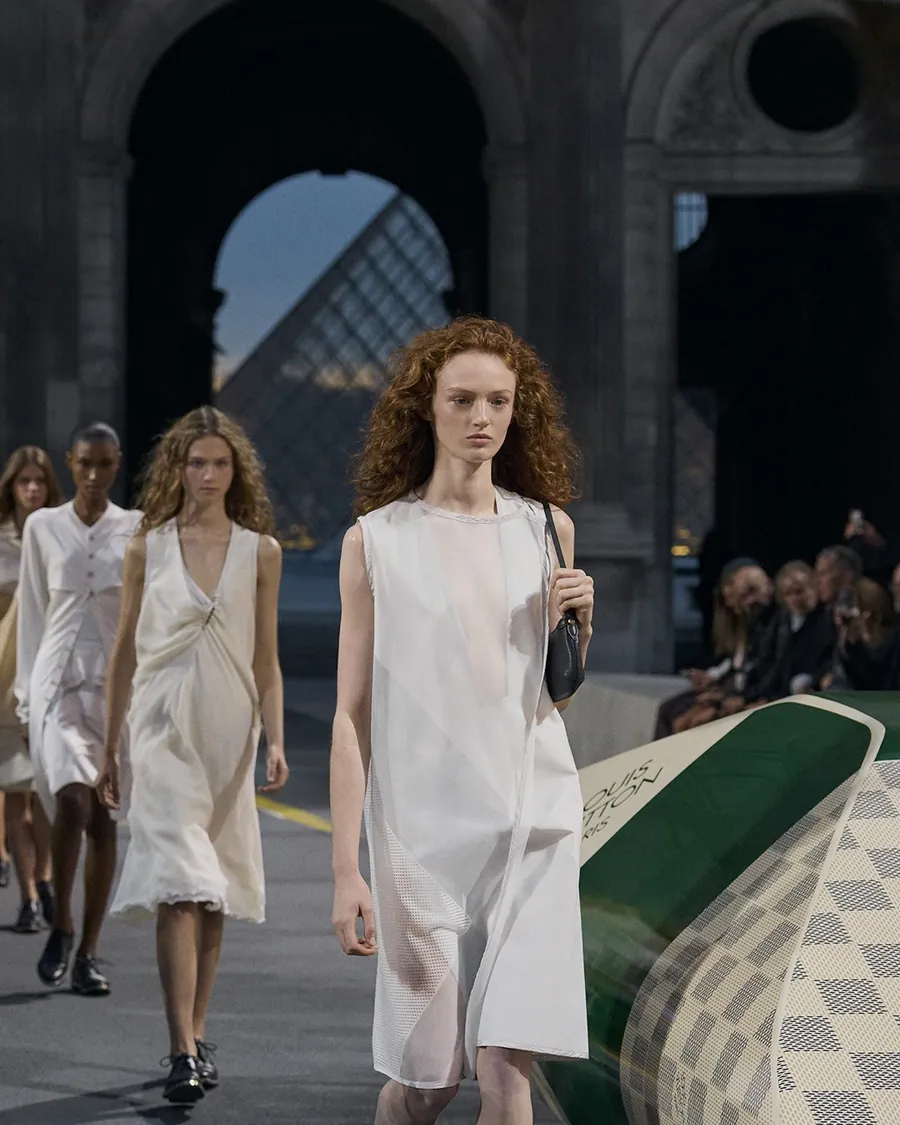 Final del desfile Louis Vuitton primavera-verano 2027: modelos con vestidos blancos ligeros en la Cour Carrée, al fondo la pirámide del Louvre