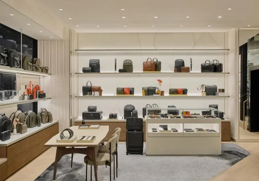 Pared de marroquinería de Montblanc con bolsos y pequeña marroquinería en estantes claros, delante una mesa de madera