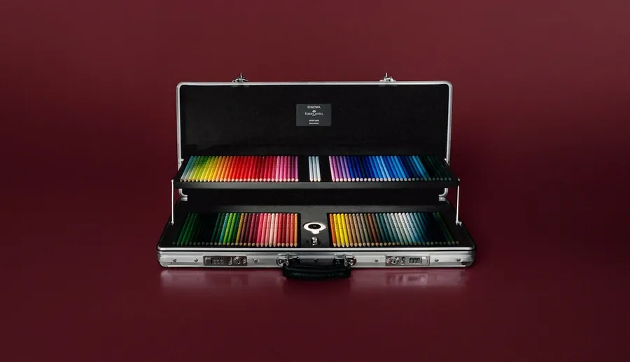 El Artist Case de RIMOWA × Faber-Castell abierto sobre fondo rojo oscuro, con sus dos bandejas llenas de lápices de colores